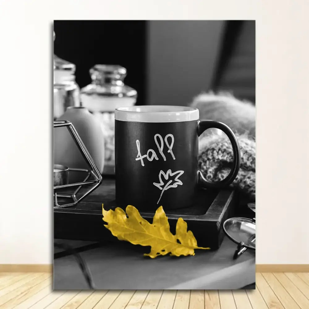 Black ceramic mug with white fall lettering and leaf design beside a yellow autumn leaf in nordic landscape canvas print set