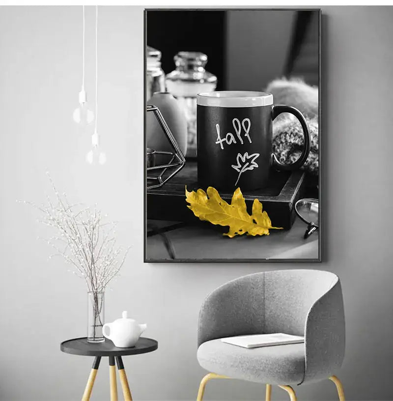 Black ceramic mug with white chalk style fall text and leaf design on dark tray beside yellow autumn leaf with nordic landscape canvas print set