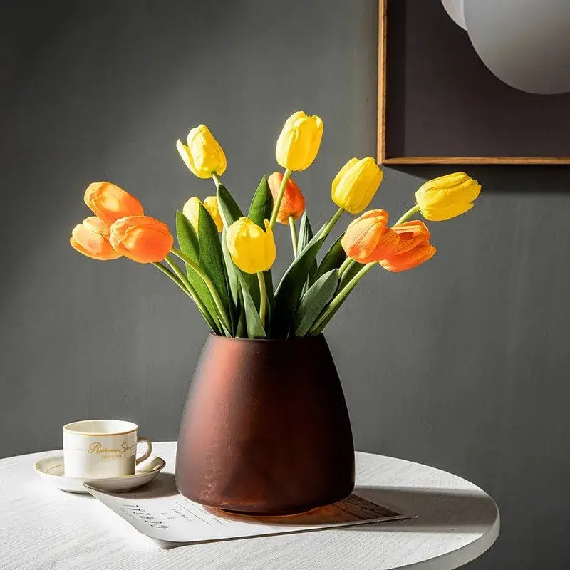 A matte copper-toned ceramic vase with yellow and orange tulips in a decorbites™ nordic luxe frosted glass vase