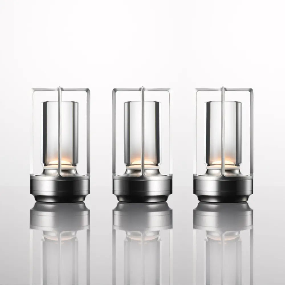 Three sleek nordic rechargeable table lamps with transparent glass cylinders and metallic frames by DecorBites™