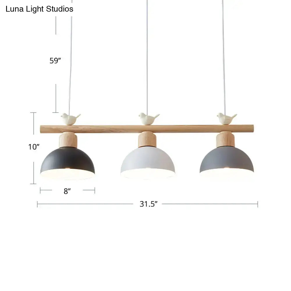 Modern three-light hanging island light with natural wood bar, black white and gray metal dome shades, and ceramic bird decor