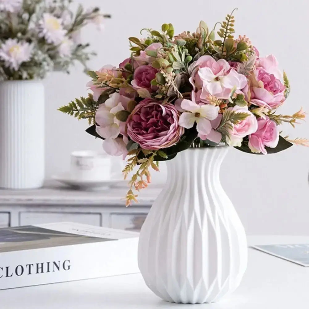 White ceramic flower vase with vertical ridged texture holding pink and mauve artificial flowers by decorbites nordic style