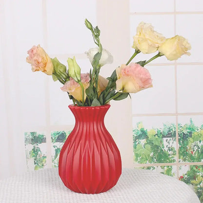A vibrant red plastic flower vase with fluted geometric pattern holding soft pink and yellow roses for home decor