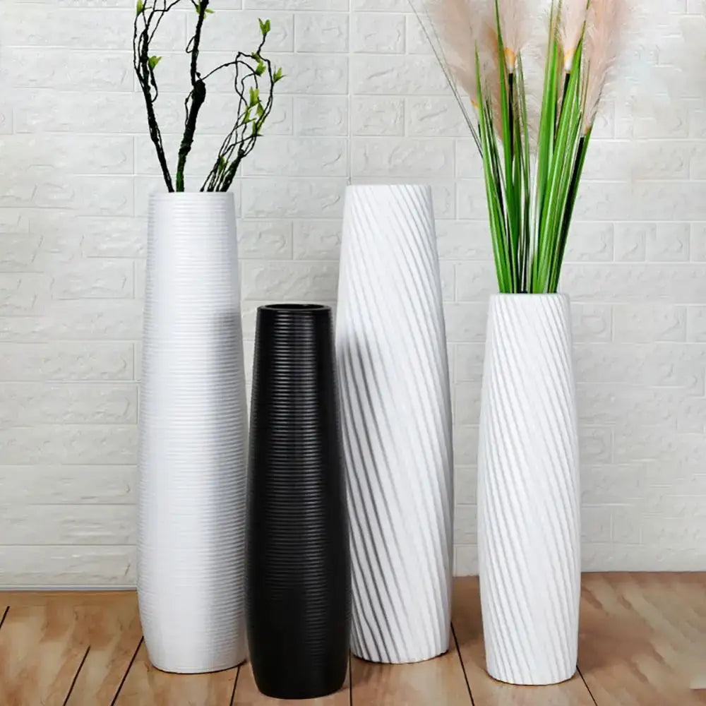 Three tall slender decorbites nordic style plastic flower vases in white and black with textured surfaces against brick wall