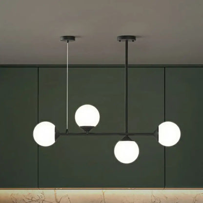 Modern black metal chandelier with four glowing white opaline glass globes for minimalist dining room island lighting