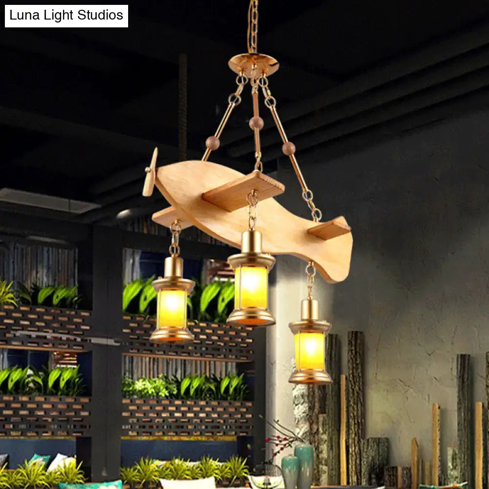 A rustic wooden airplane-shaped pendant light with brass accents and three orange glass lanterns featuring fish guitar design
