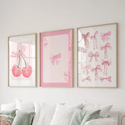 Three framed pink bows wall art set with cherries and playing cards prints displayed above a bed by DecorBites™