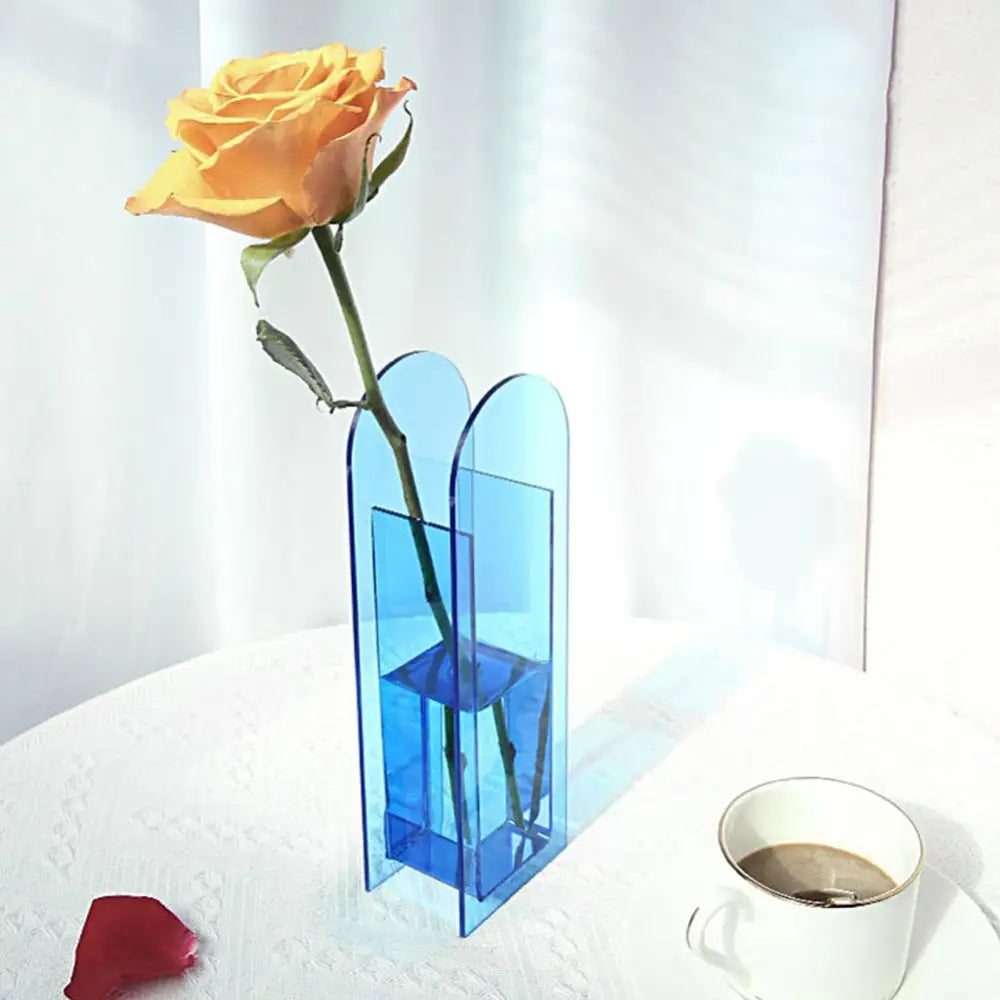 A translucent blue rainbow color acrylic flower vase in nordic style holding a single yellow rose