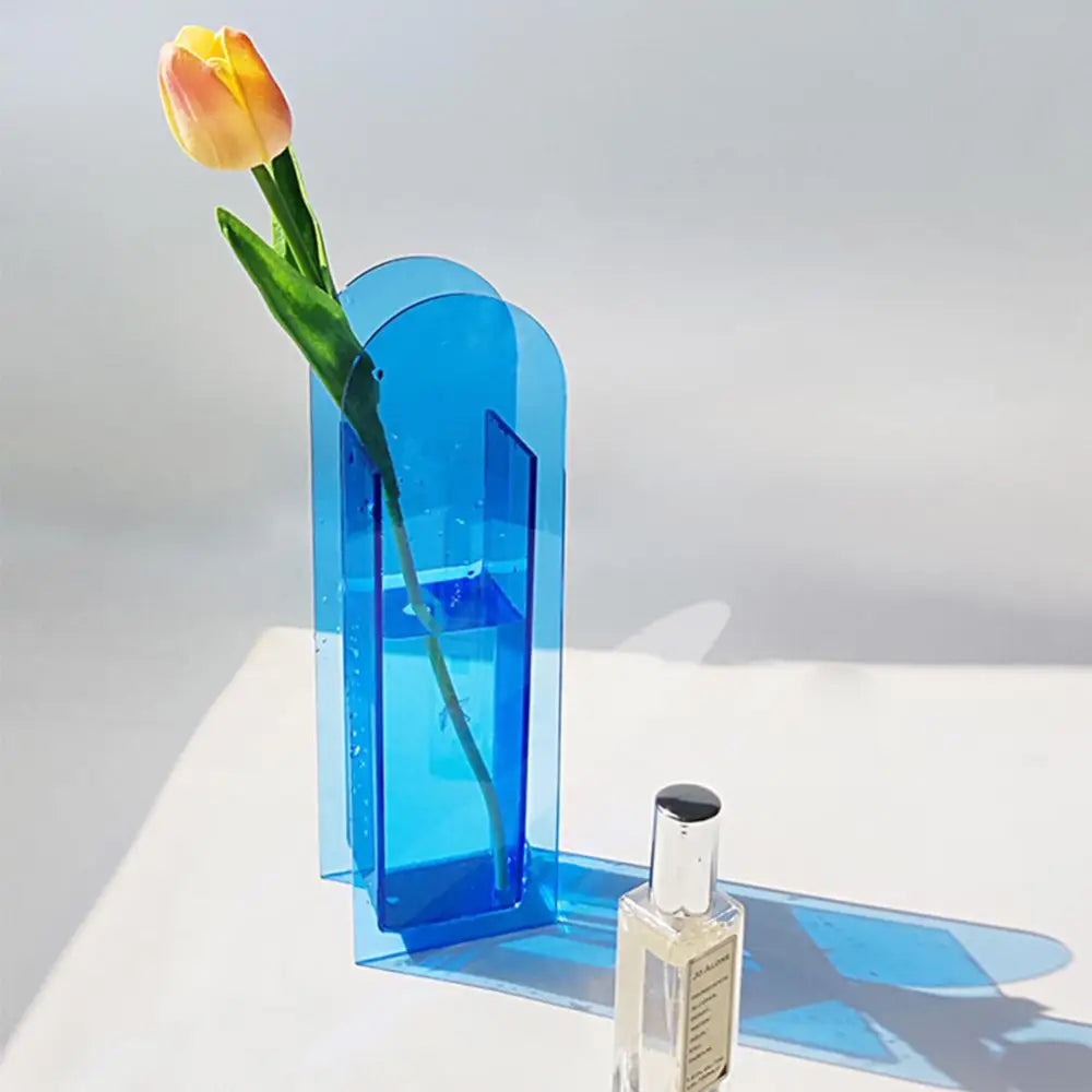 A translucent blue rainbow color acrylic flower vase with a nordic style arched design holding a yellow orange tulip