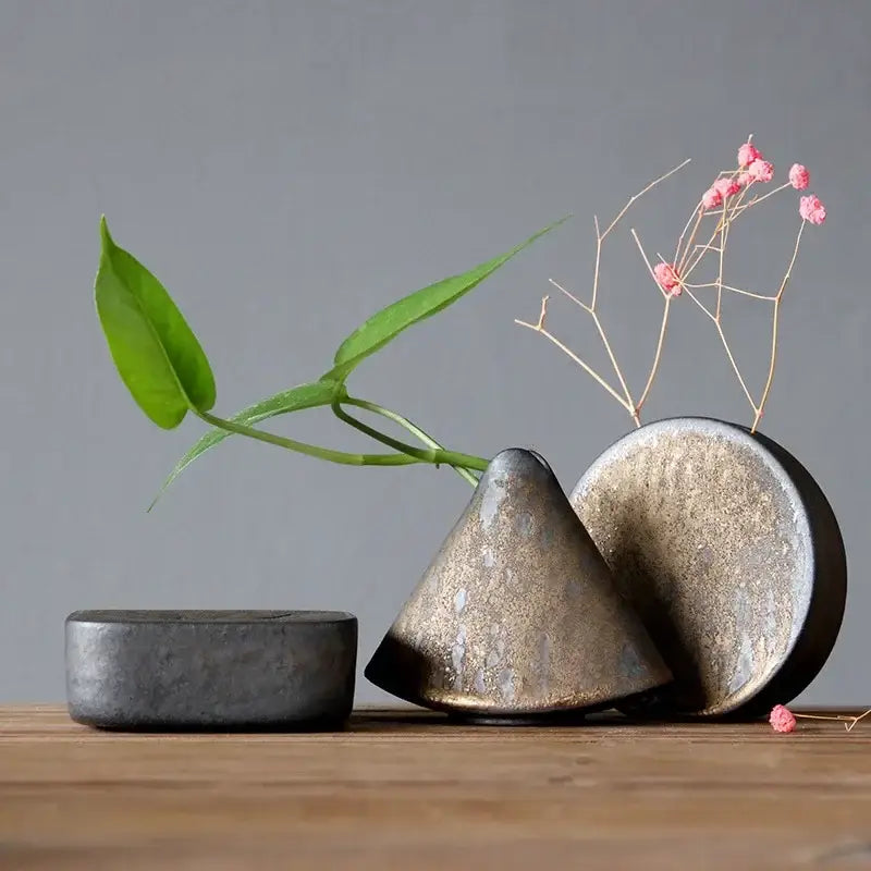 A matte-finished ceramic pottery vase ornament with conical shape and metallic glaze holding pink flowers for tea ceremony