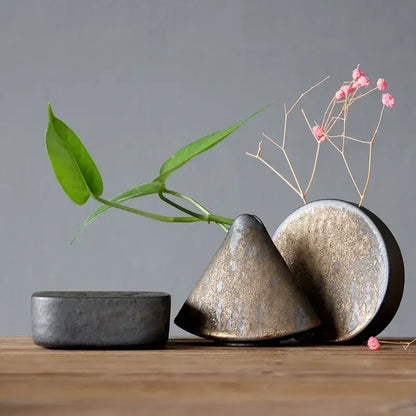 A matte-finished ceramic pottery vase ornament with conical shape and metallic glaze holding pink flowers for tea ceremony