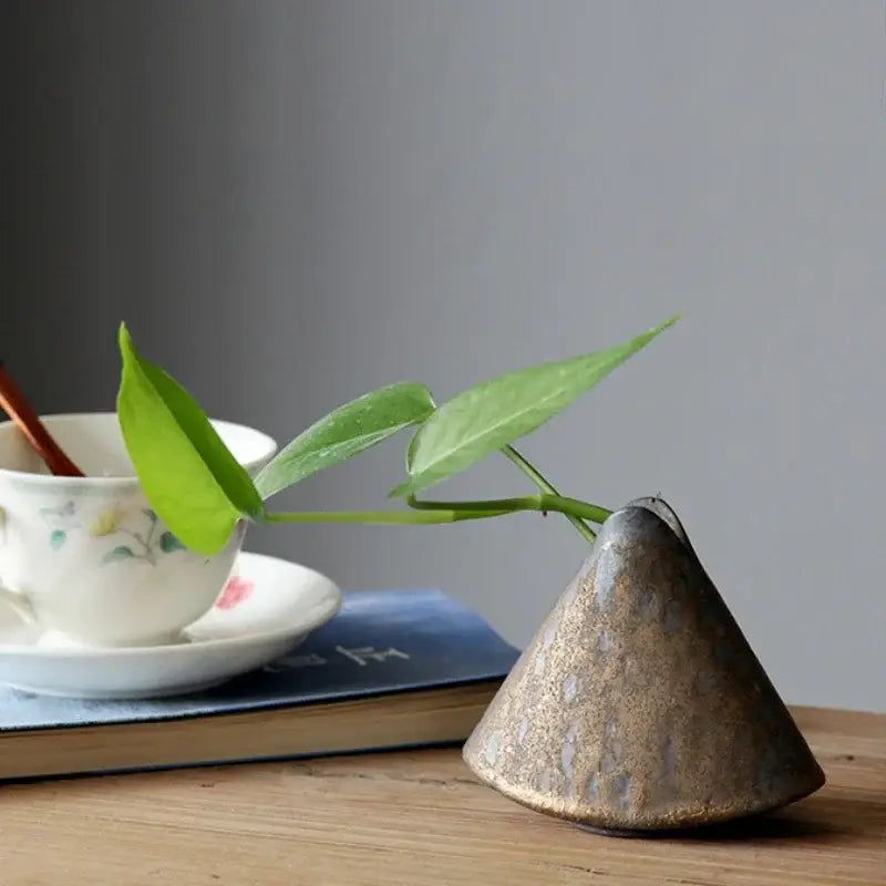 A rustic cone-shaped pottery vase ornament with textured earthy brown glaze holding a single green leaf for tea ceremony decor