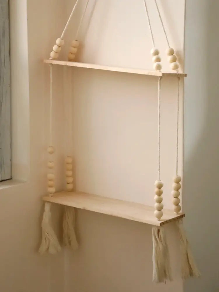 A rustic wooden wall shelf by DecorBites with natural wood finish, beige rope suspension, and decorative tassels