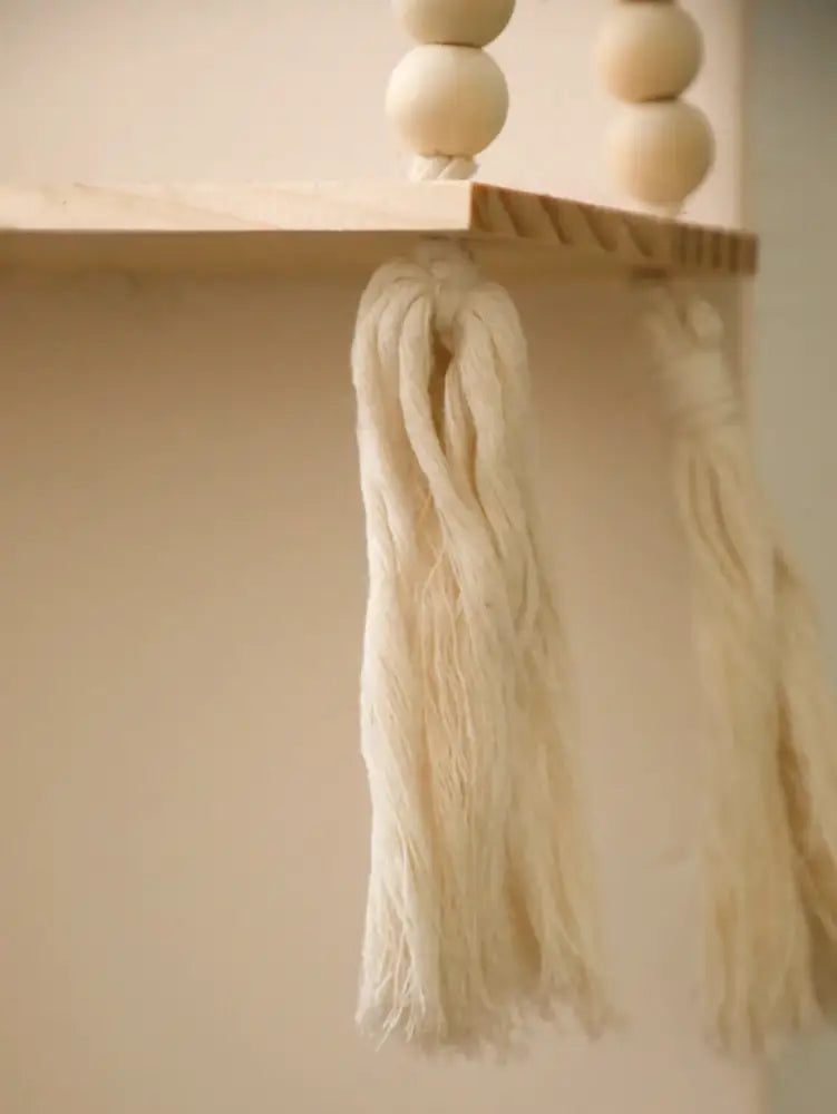 Cream-colored macrame tassels hanging from a rustic wooden wall shelf with hanging plant storage by decorbites