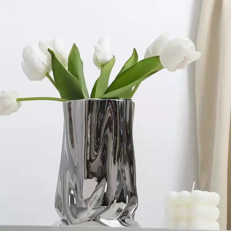 A sleek silver ruffled ceramic flower vase by DecorBites holding white tulips with a fluid sculpted design