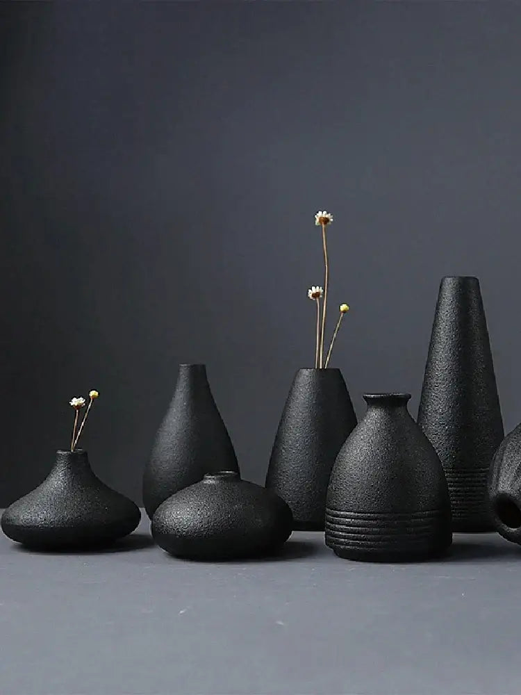 A collection of matte black ceramic small vases with textured surfaces holding dried flowers for elegant japanese home decor
