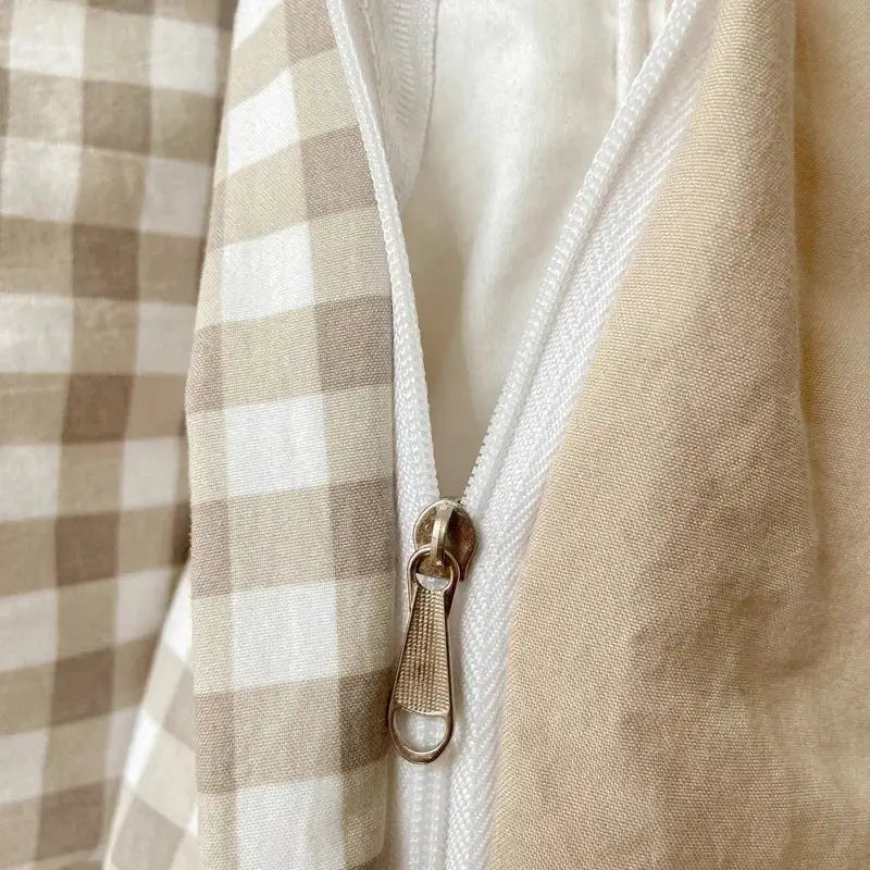 A gold-toned zipper with textured pull tab on beige and white gingham fabric of DecorBites™ pcs duvet cover set