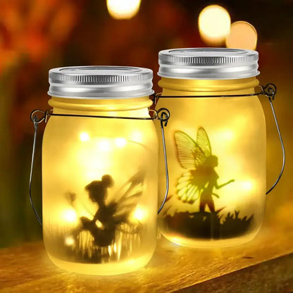 Two illuminated glass solar mason jar lanterns with silver lids and fairy silhouette led lights for garden decoration