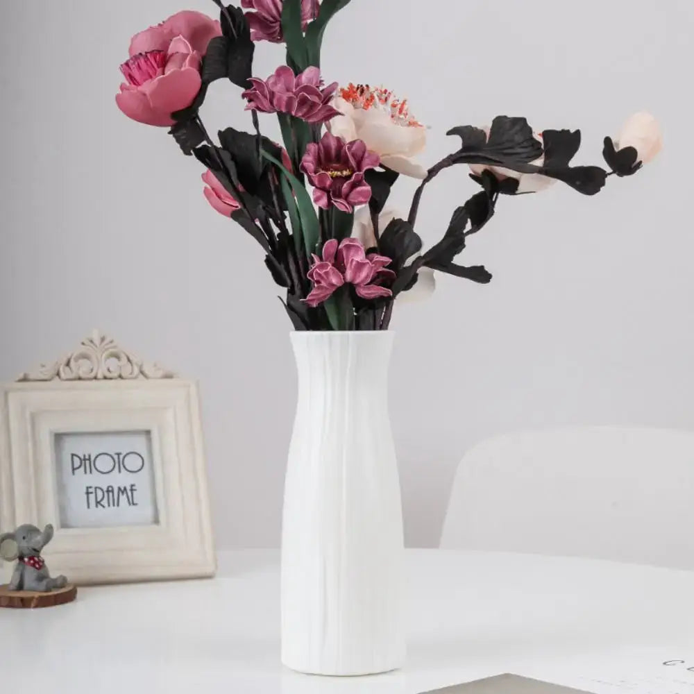 White ceramic solid color plastic flower vase with vertical ridged texture holding pink purple and cream artificial flowers