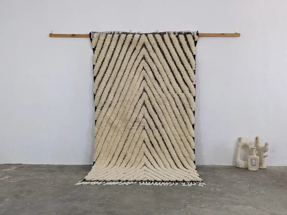 Cream-colored textured wool tapis beni ouarain with bold black zigzag stripes and fringed edges by decorbites