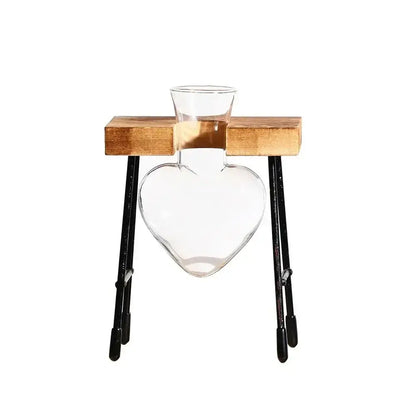 Clear glass heart-shaped vase with narrow neck on wooden platform with metal legs for avocado seed starter use