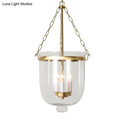 Gold-toned brass pendant lantern with clear glass body and inverted cloche design featuring chain cord length