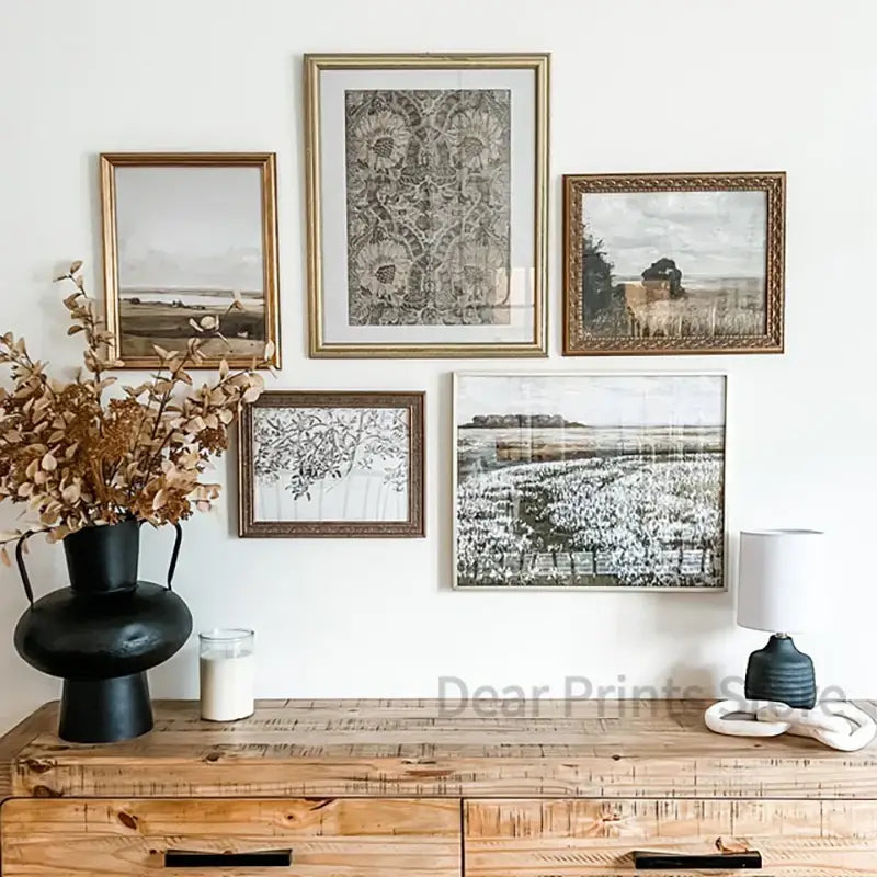 Set of five framed black and white vintage farmhouse landscape oil paintings with gold frames above wooden console table
