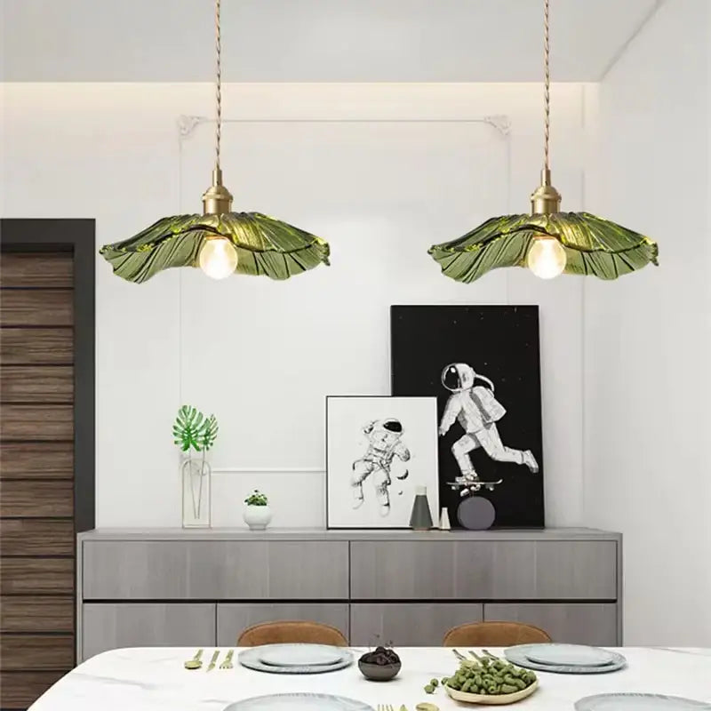Two green leaf-shaped DecorBites™ pendant lights with brass fixtures hang above a dining table for home decor