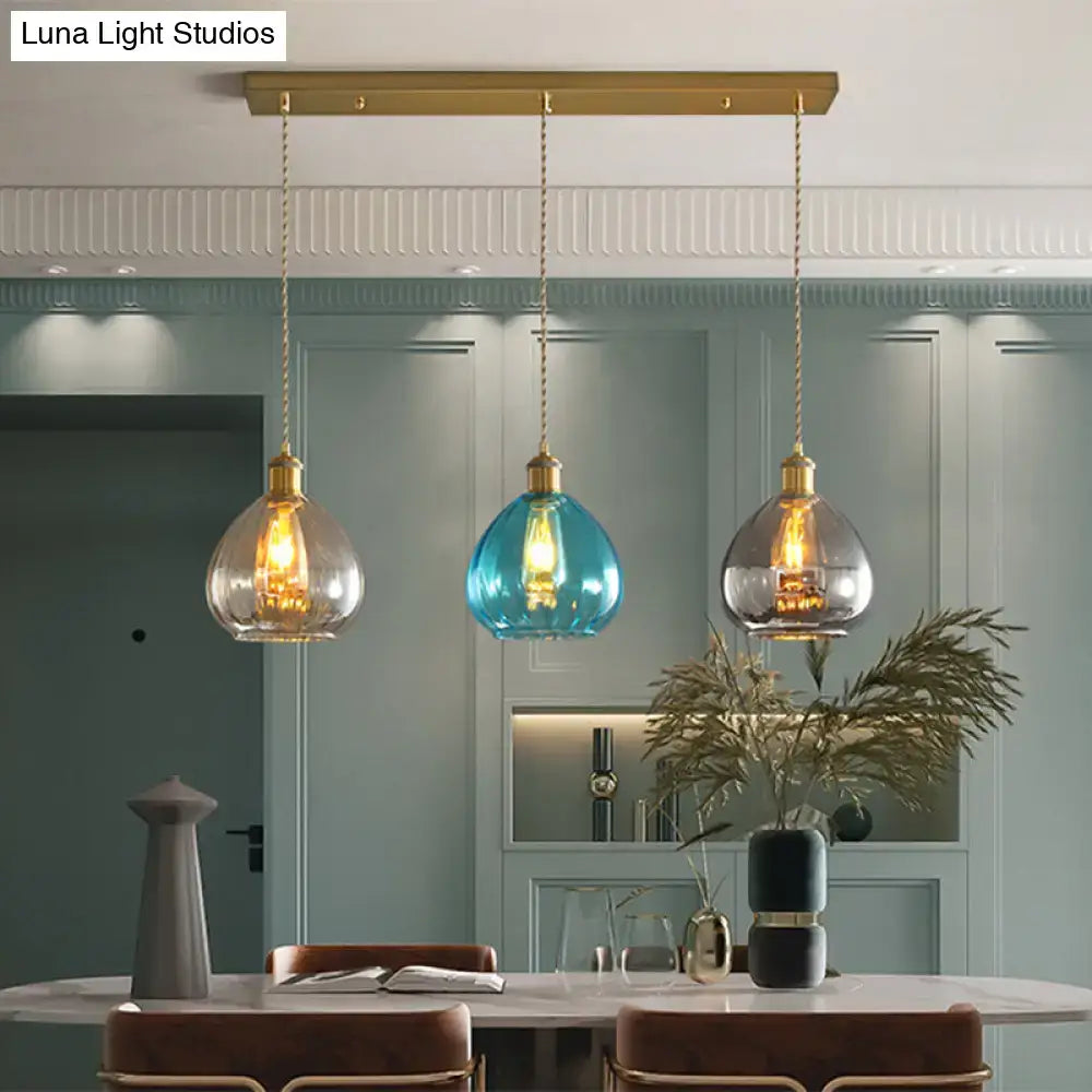 Three pendant lights with glass onion multi shades in tan blue grey and brass fixtures on a multi ceiling light bar