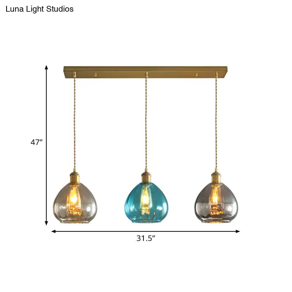 Three brass glass onion multi pendant lights with clear teal and smoky gray shades on a 47-inch bar for ceiling use