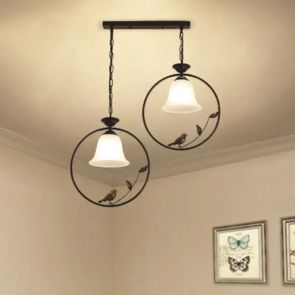 Two black wrought iron pendant lights with decorative bird accents and handblown glass flared shades for kitchen island lighting