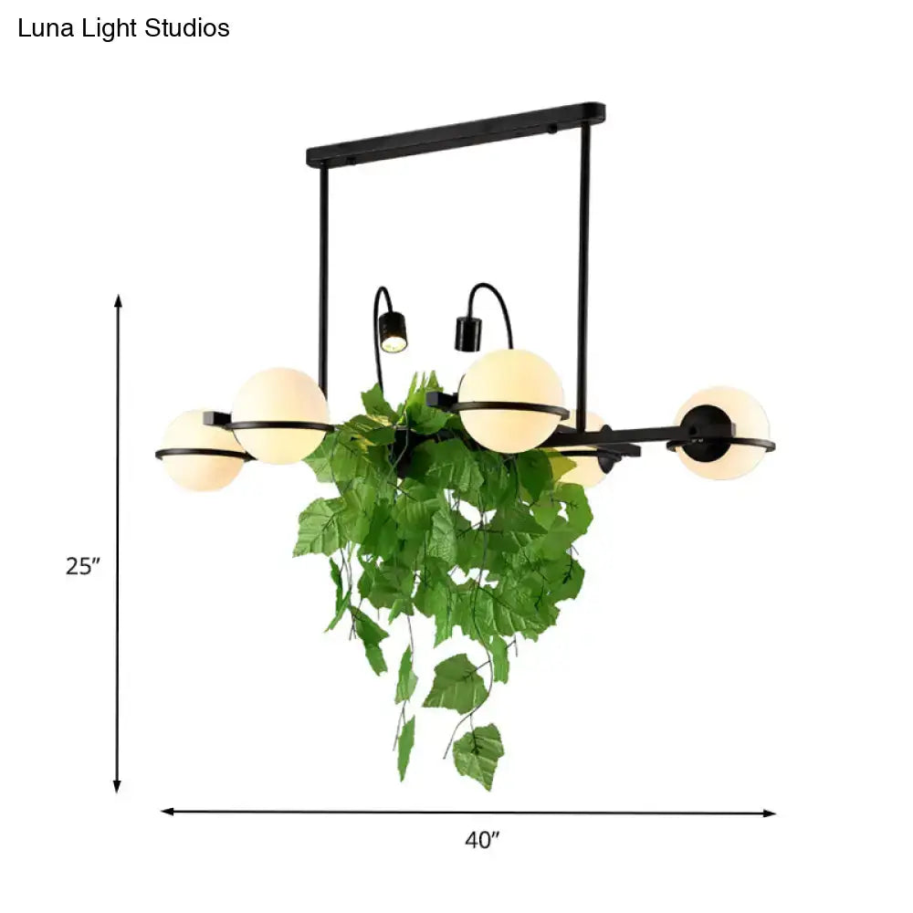 Black metal chandelier island lighting fixture with five frosted glass globes and hanging green vine by DecorBites™