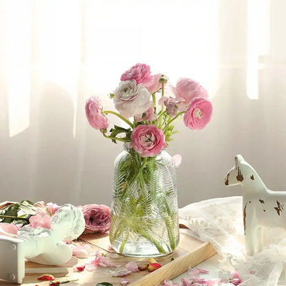 A clear glass vintage relief vase with textured leaf design holds pink and white ranunculus for hydroponic plants