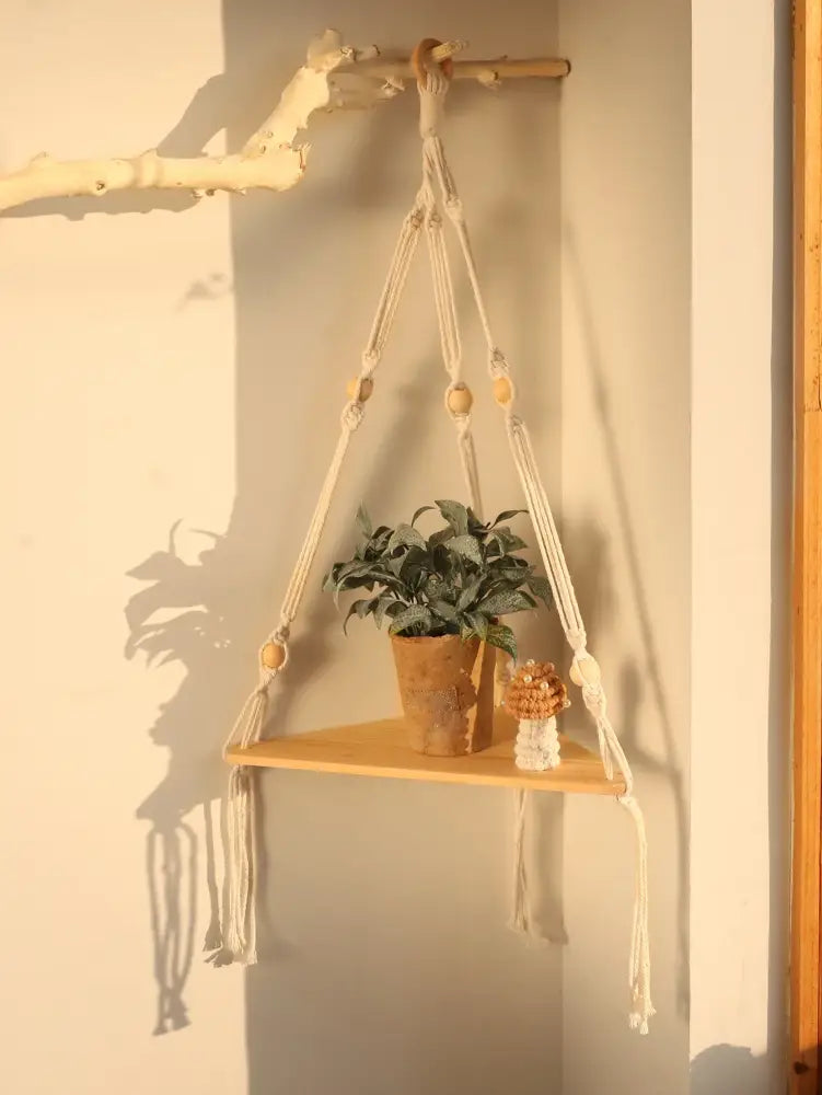 Beige macrame wooden corner shelf with beads and tassels holding a potted plant by decorbites boho wall decor