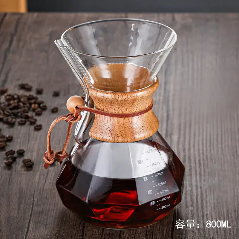 Clear glass hand brew coffee maker with wooden collar filled with dark red coffee from diamond glass hand set