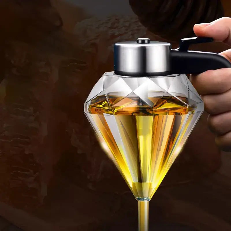 Diamond glass syrup honey dispenser with silver lid and black handle filled with golden-yellow oil liquid
