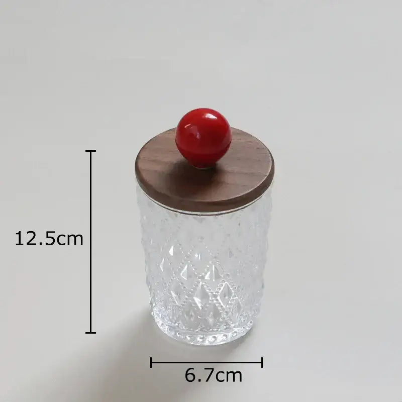 Clear glass jewelry jar with diamond pattern and walnut lid topped by a glossy red colorful ceramic ball knob