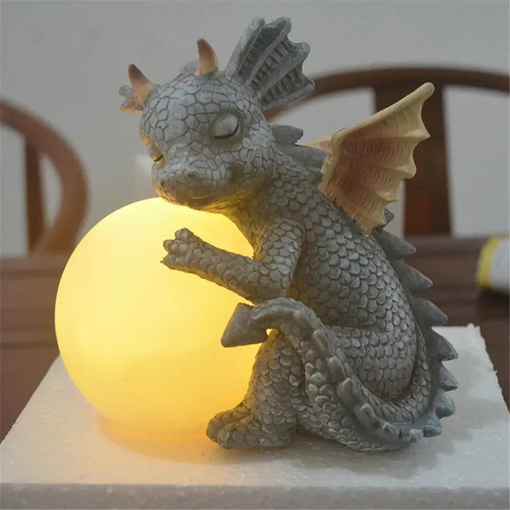 Gray dragon dino garden sculpture with textured scales and yellow wings hugging a glowing lamp for outdoor decorbites decor