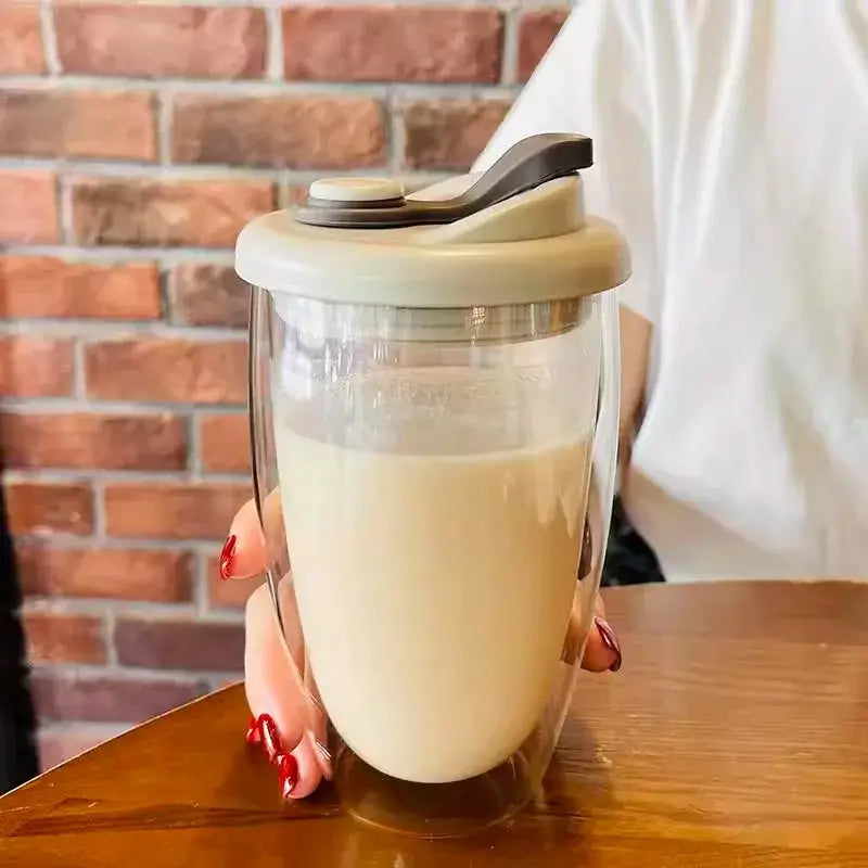Clear double deck insulated glass travel mug with beige lid and black flip-top spout filled with milk