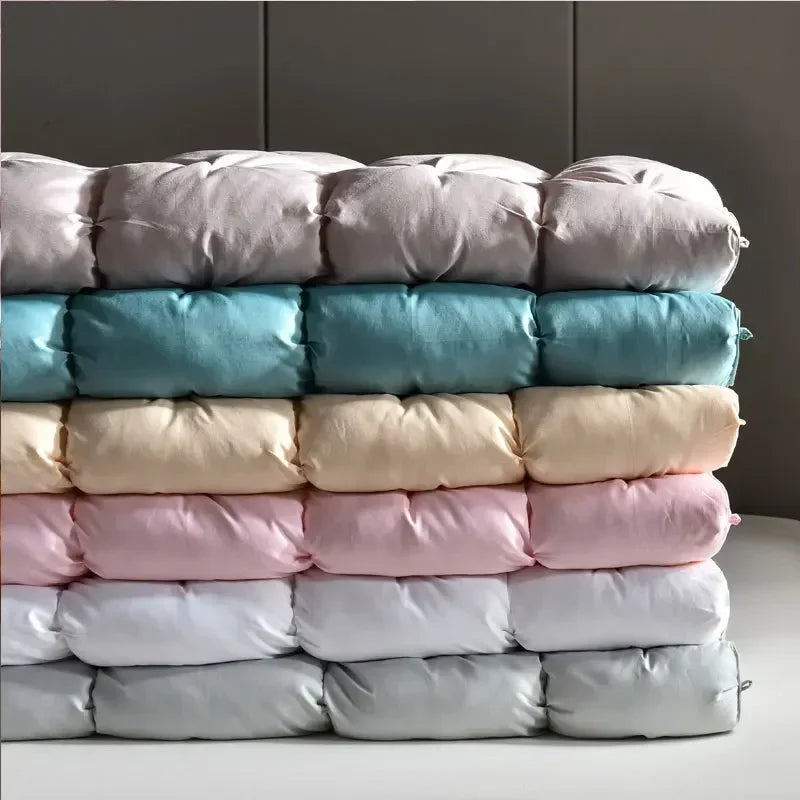 Stack of plush quilted down duvets in pastel lavender teal cream pink and gray filled with 95 white goose down