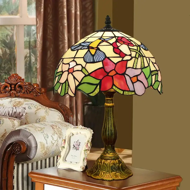 A decorbites dragonfly tiffany stained glass table lamp with multicolored floral and hummingbird panels on a brass base