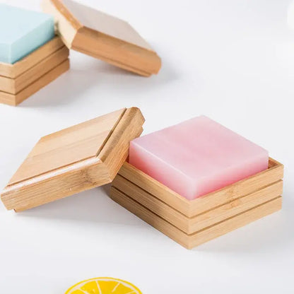 Pink translucent soap bar nestled in a light wood bamboo soap dish with hinged lid for bathroom storage