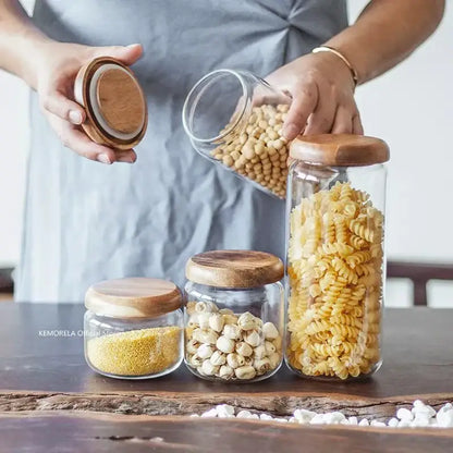 Clear glass storage jars with elegant acacia wood lids holding dry goods like pasta and grains for kitchen use