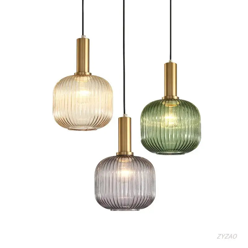 Three modern glass pendant lights with amber, green, and gray ribbed shades and brass metal stems for dining rooms
