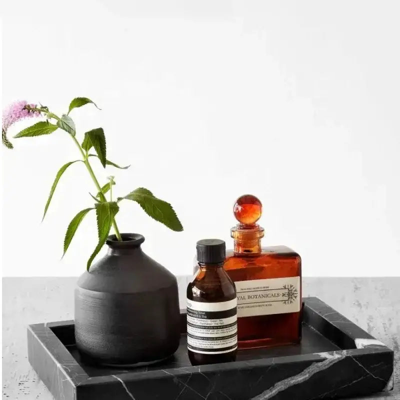Elegant black and white afralia marble tray with a black matte ceramic vase holding a pink flower and green leaves