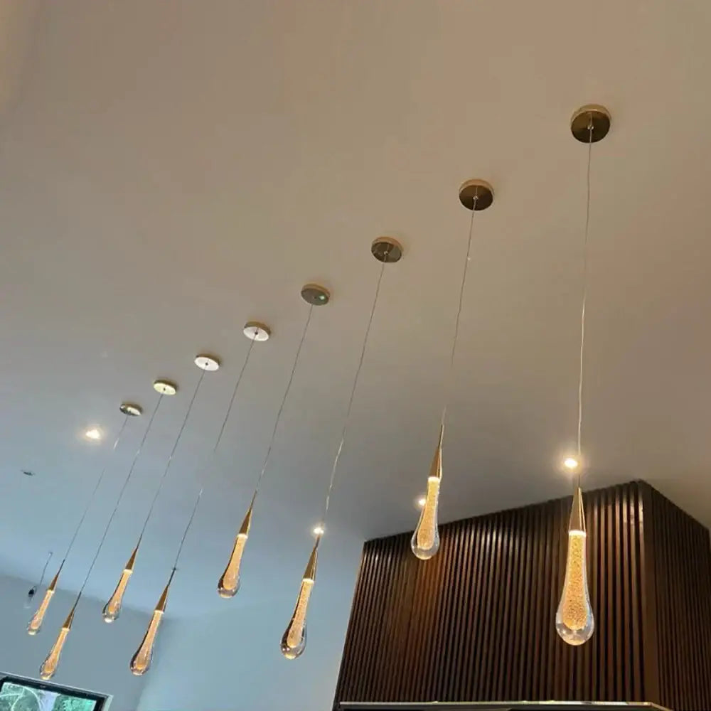 A modern teardrop-shaped crystal glass led pendant light with golden LED and brass accents for dining room decorbites