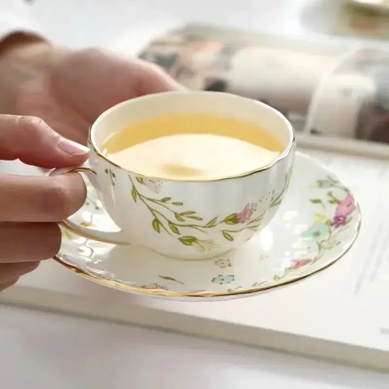 A delicate white porcelain teacup with elegant gold flower trim filled with yellow tea in a decorbites saucer set