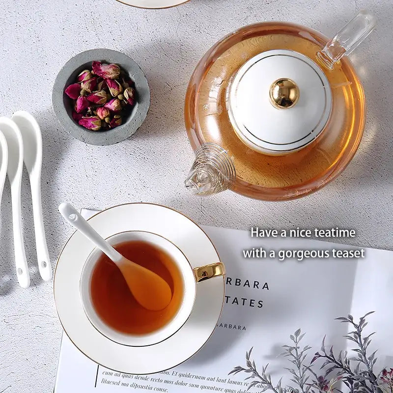 Clear glass teapot with white ceramic lid and gold-toned handle filled with amber tea in decorbites gold white tea set