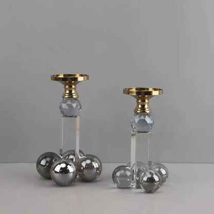 A pair of elegant clear crystal geometric candle holders with gray spheres and gold-toned tops on acrylic bases