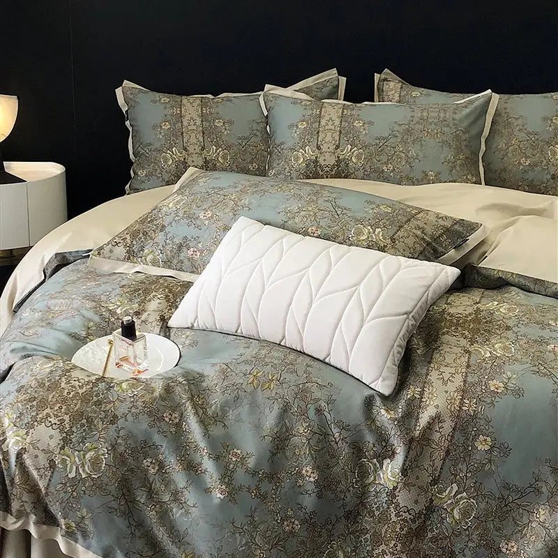 A white quilted pillow with diamond stitching on a bed featuring an elegant teal and gold floral luxury bedding set